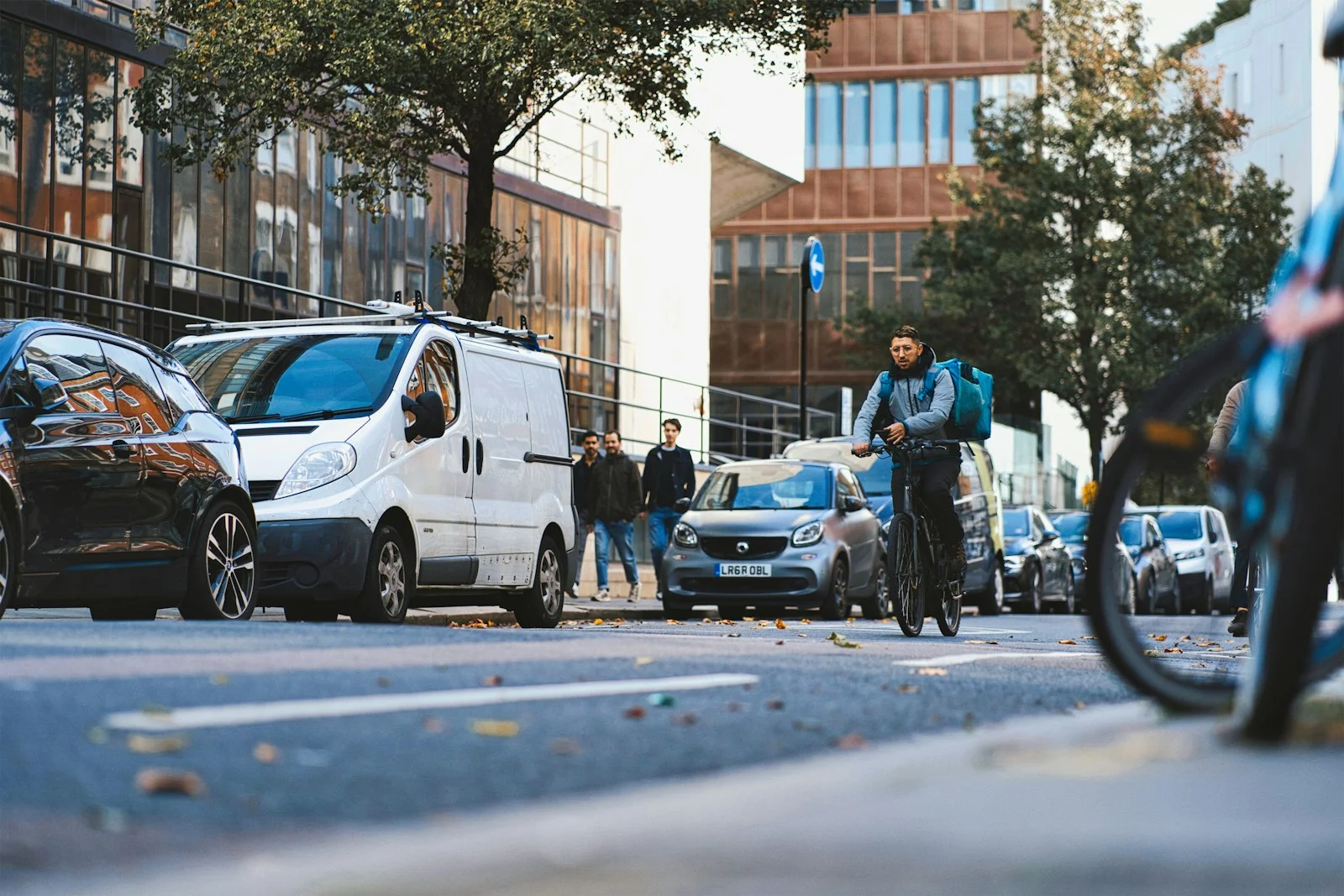 a man riding a bike down a street next to parked cars a man riding a bike down a street next to parked cars